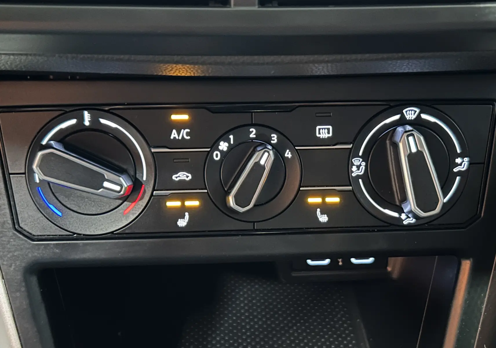 Gros plan sur les commandes de climatisation avec voyants allumés dans l’habitacle noir d’une Volkswagen Polo 2022.
