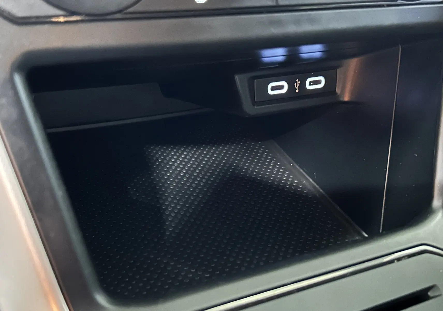 Gros plan sur la console centrale d'une Volkswagen Polo noire, montrant deux ports USB lumineux et un espace de rangement.