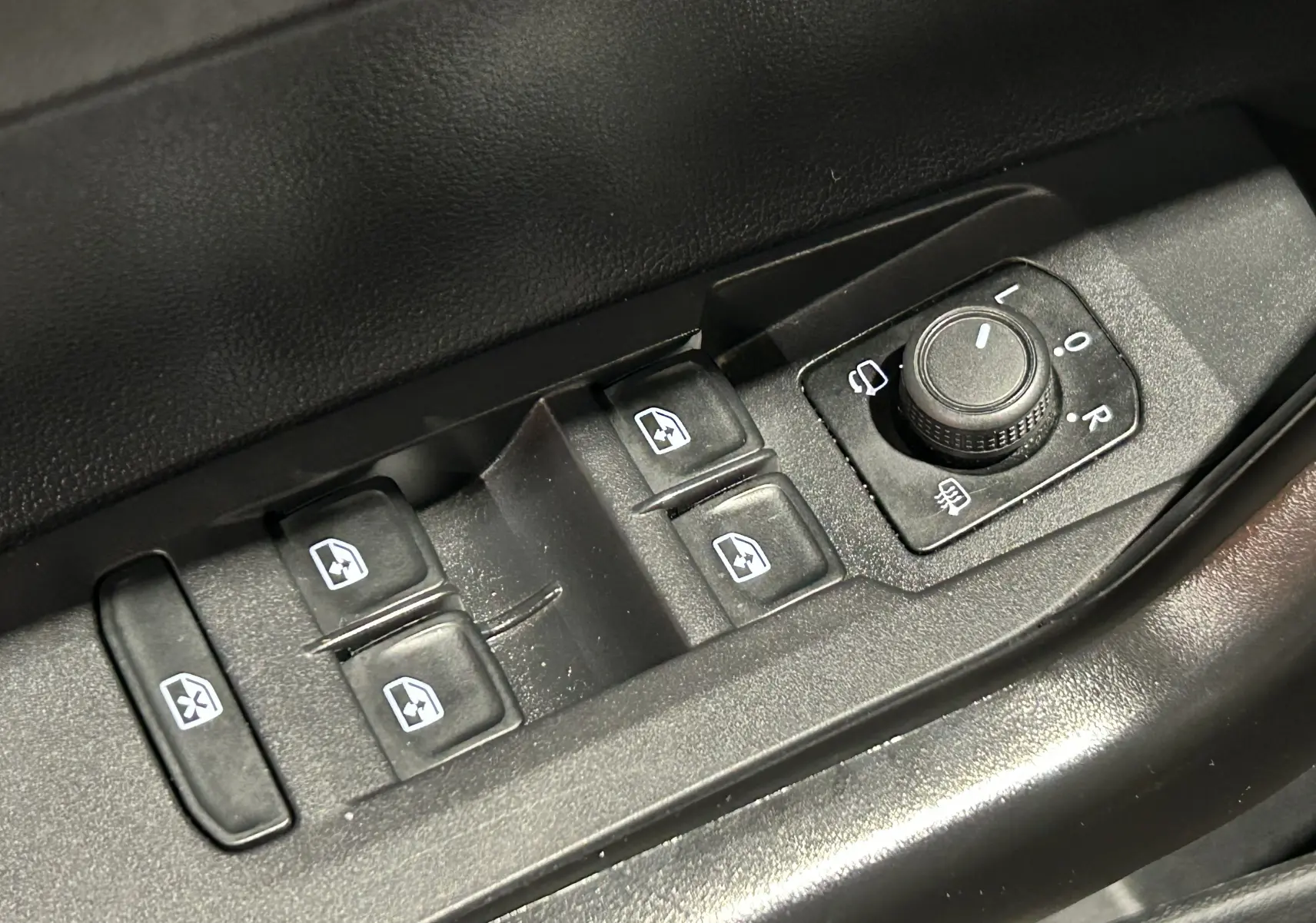 Gros plan sur les commandes de lève-vitres et réglage des rétroviseurs côté conducteur d’une Volkswagen Polo noire.