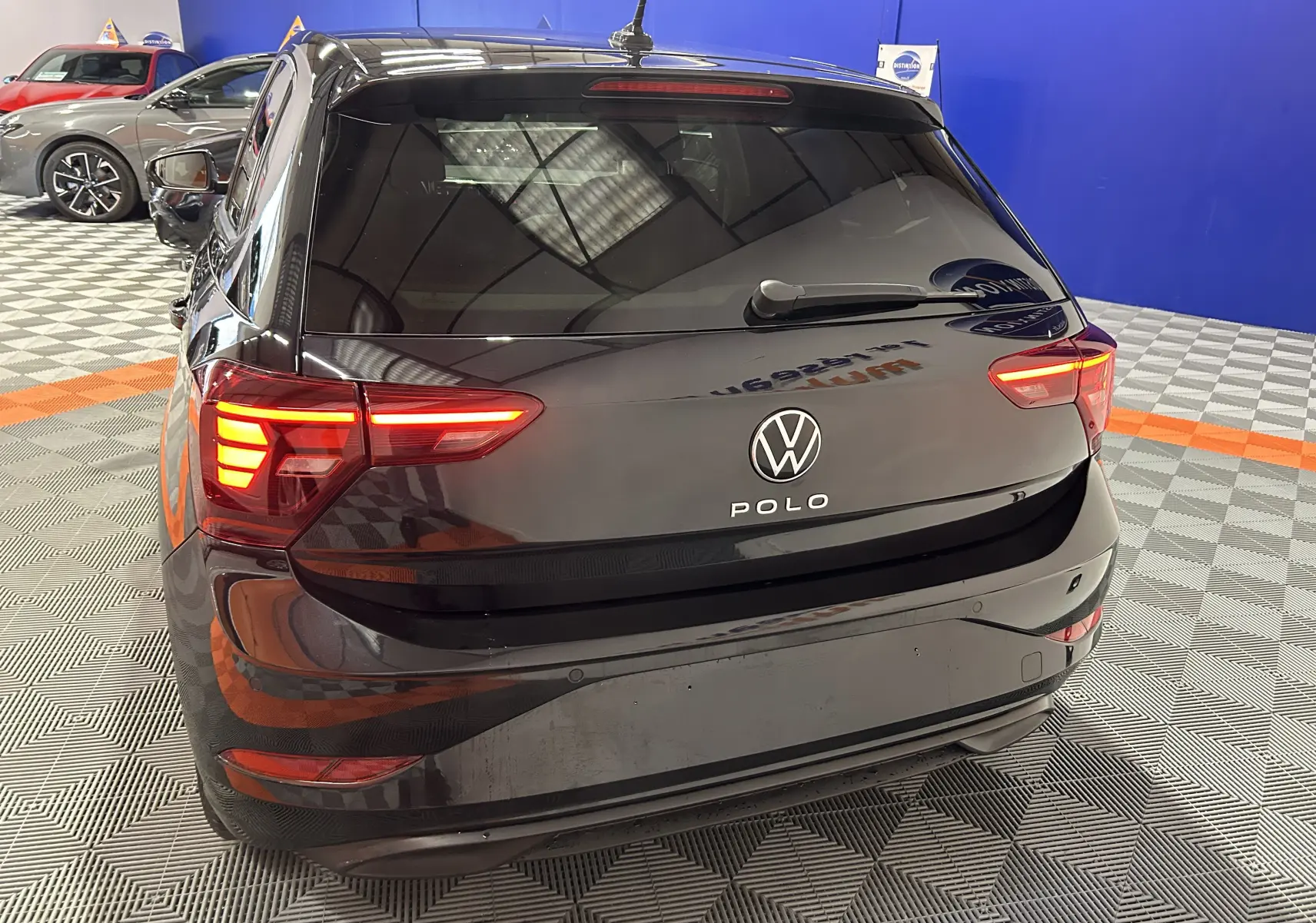 Vue 3/4 arrière d'une Volkswagen Polo noire 2022 avec feux arrière allumés dans un showroom.