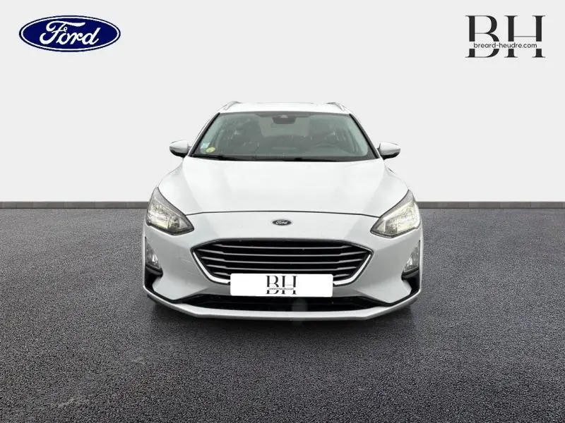 Vue de face d'une Ford Focus SW 1.5 EcoBlue blanche Glacier, avec calandre noire et phares allumés.