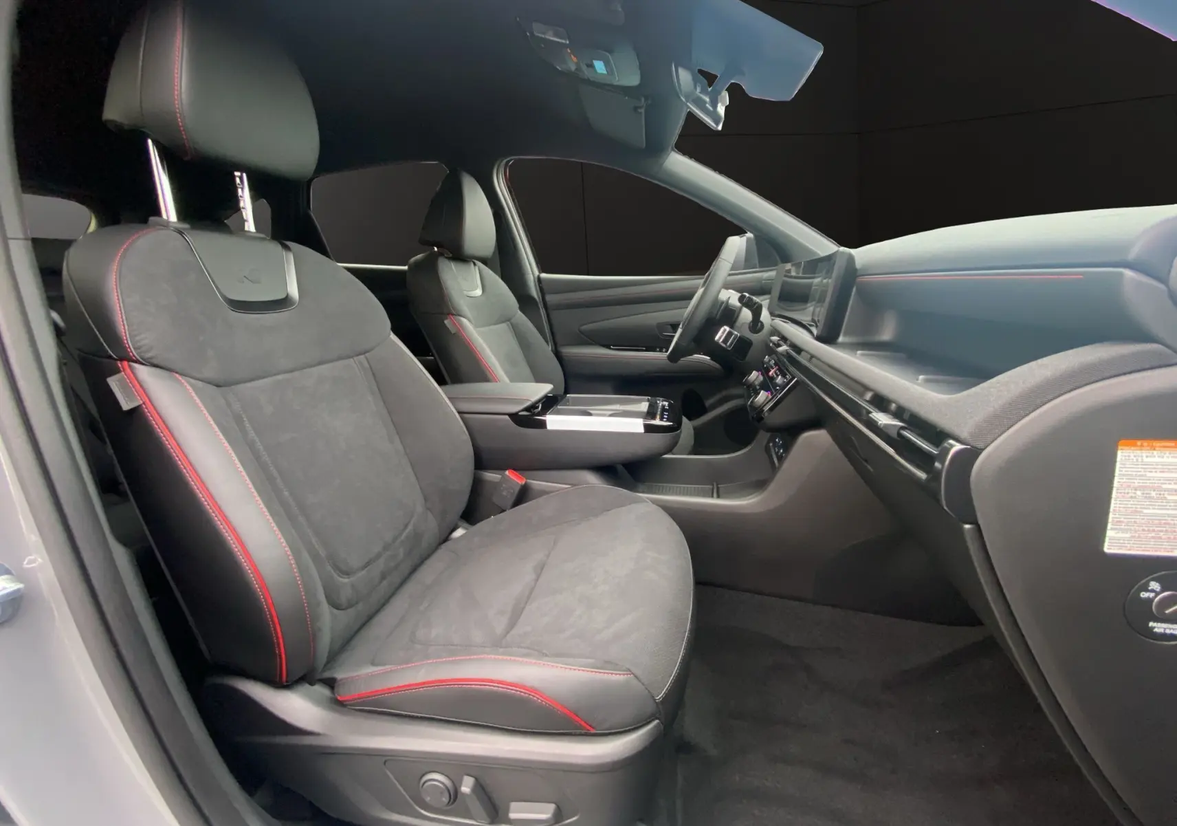 Intérieur du Hyundai Tucson 2026 vu côté droit, sièges cuir/Alcantara noirs avec surpiqûres rouges et console centrale.