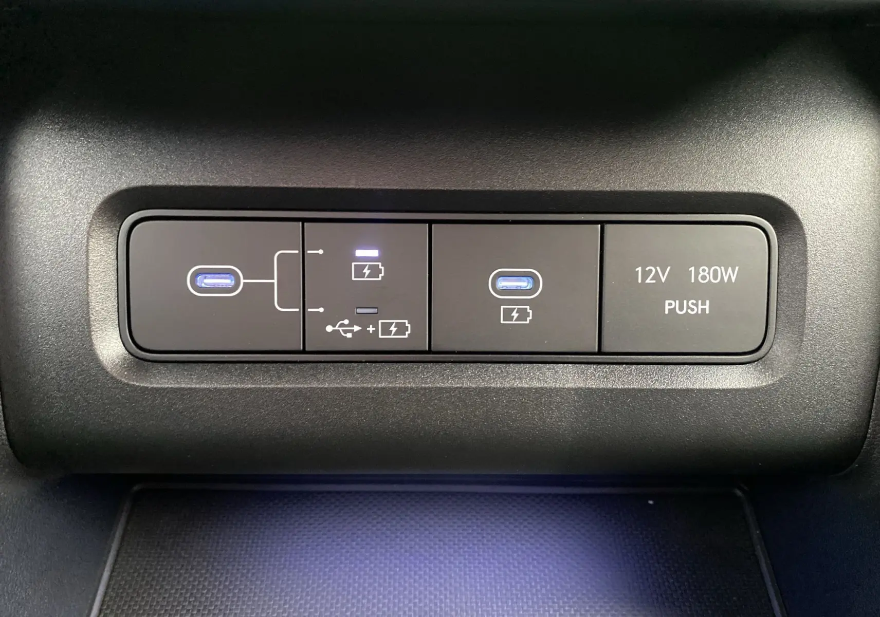 Gros plan sur les ports USB et prise 12V du Hyundai Tucson 2026 gris Shadow, avec éclairage bleu subtil.