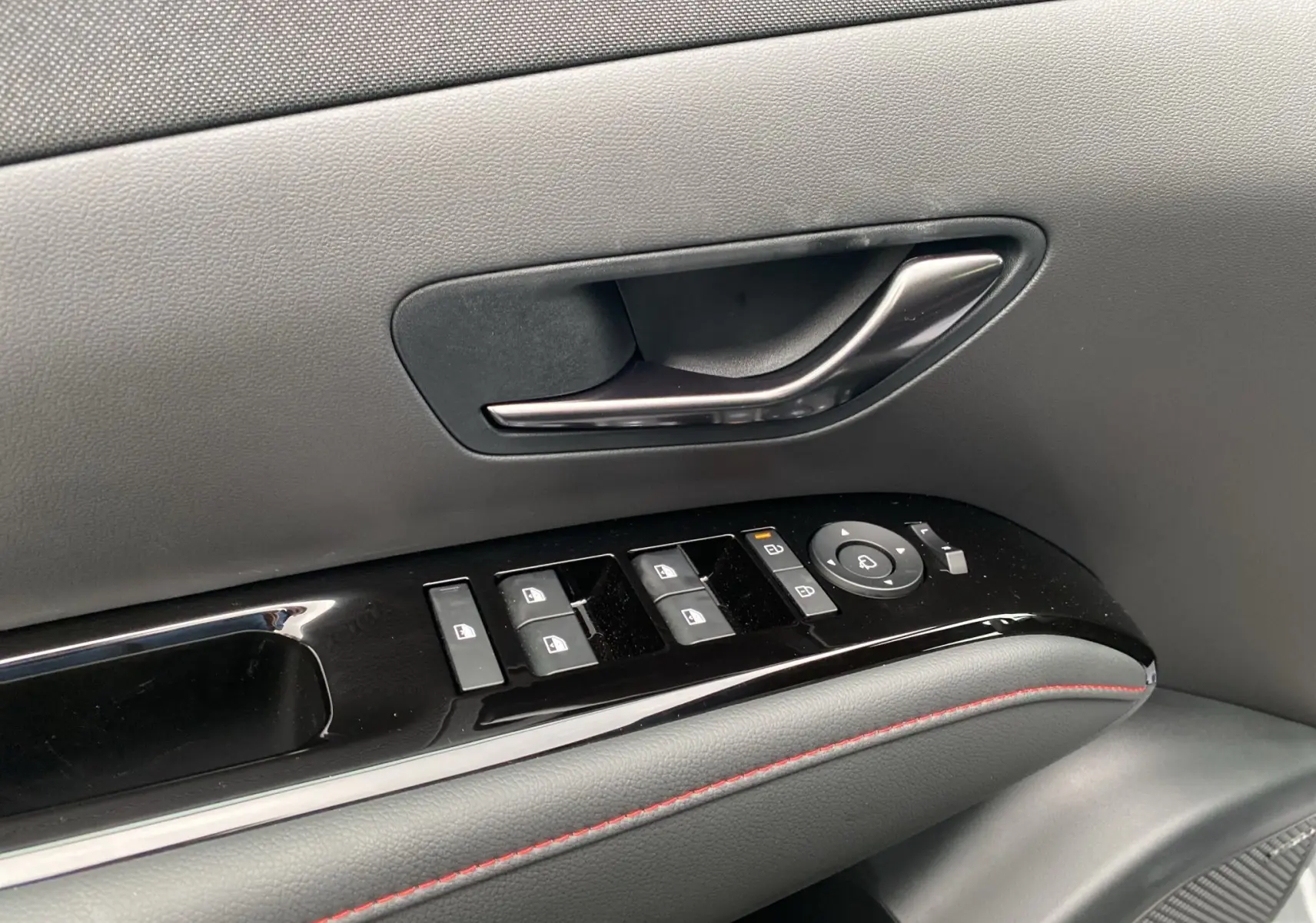 Gros plan sur la poignée intérieure et les commandes de vitres côté gauche du Hyundai Tucson gris avec surpiqûres rouges.