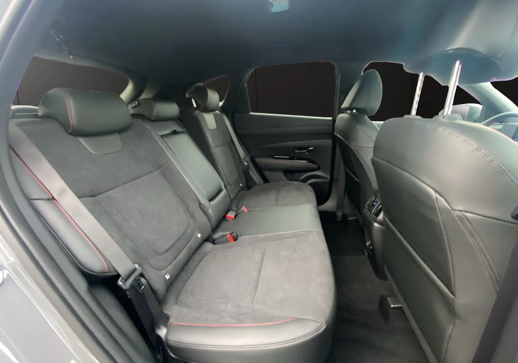 Vue intérieure arrière du Hyundai Tucson 2026 en Grey Shadow, sièges cuir noir/Alcantara avec surpiqûres rouges et vitres surteintées.