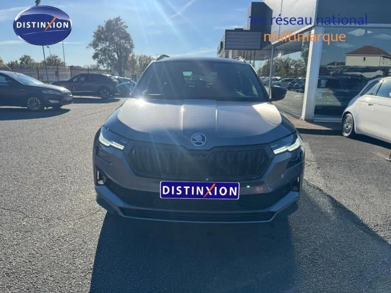 Vue de face d'un Skoda Karoq gris perle 2025 avec calandre noire et phares LED allumés en extérieur.