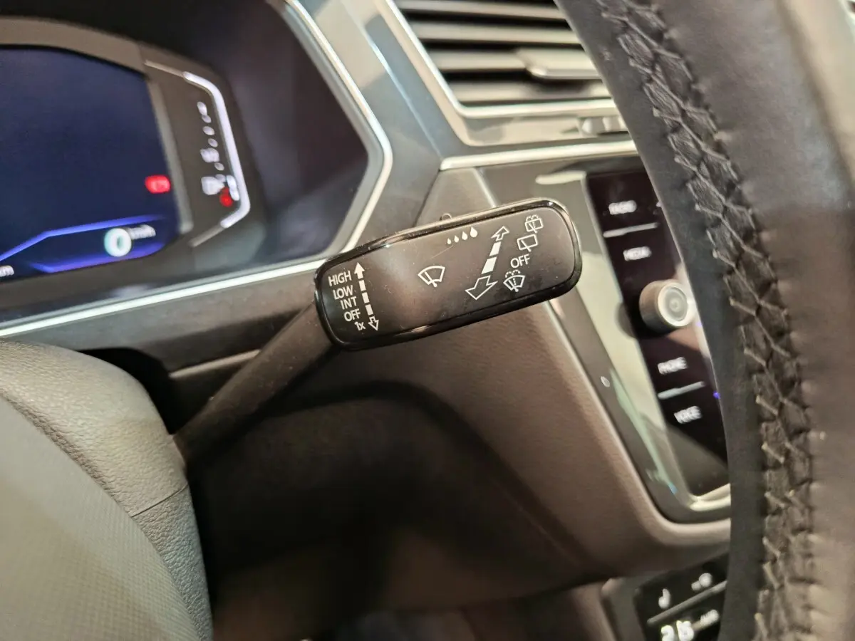 Gros plan sur le commodo d’essuie-glace noir dans l’habitacle du Volkswagen Tiguan noir, avec tableau de bord digital en arrière-plan.