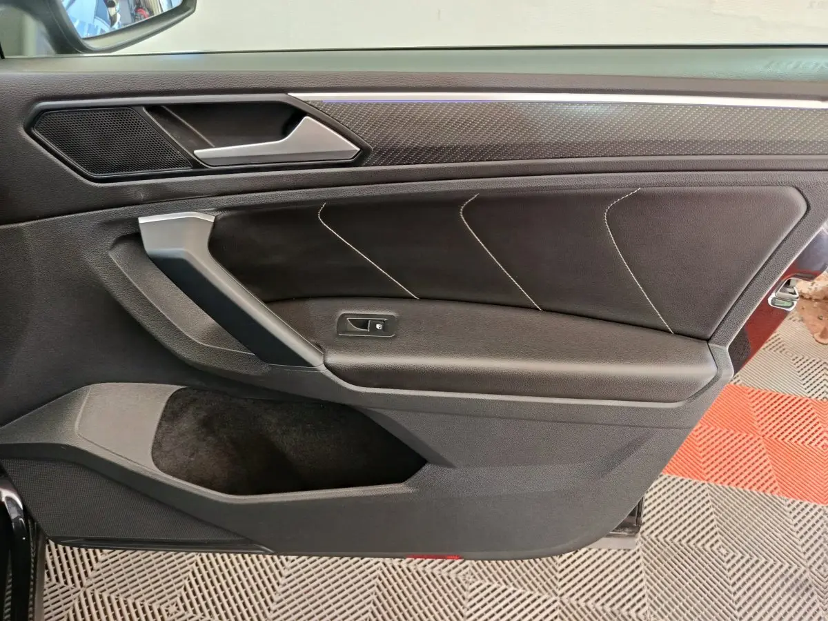 Gros plan sur la porte intérieure côté gauche du Volkswagen Tiguan noir, avec surpiqûres et poignée argentée.