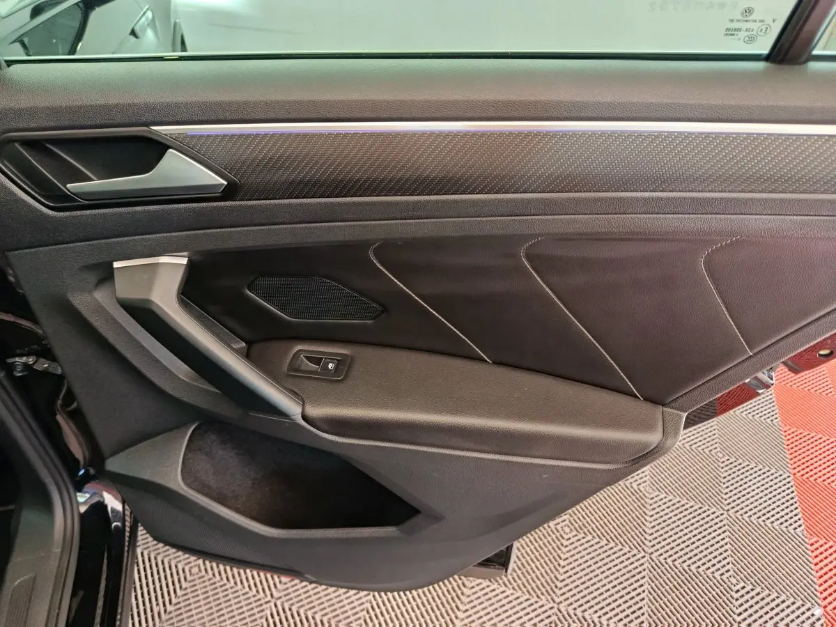 Vue intérieure côté gauche de la porte avant noire du Volkswagen Tiguan 2023 avec garniture cuir et bouton de vitre électrique.