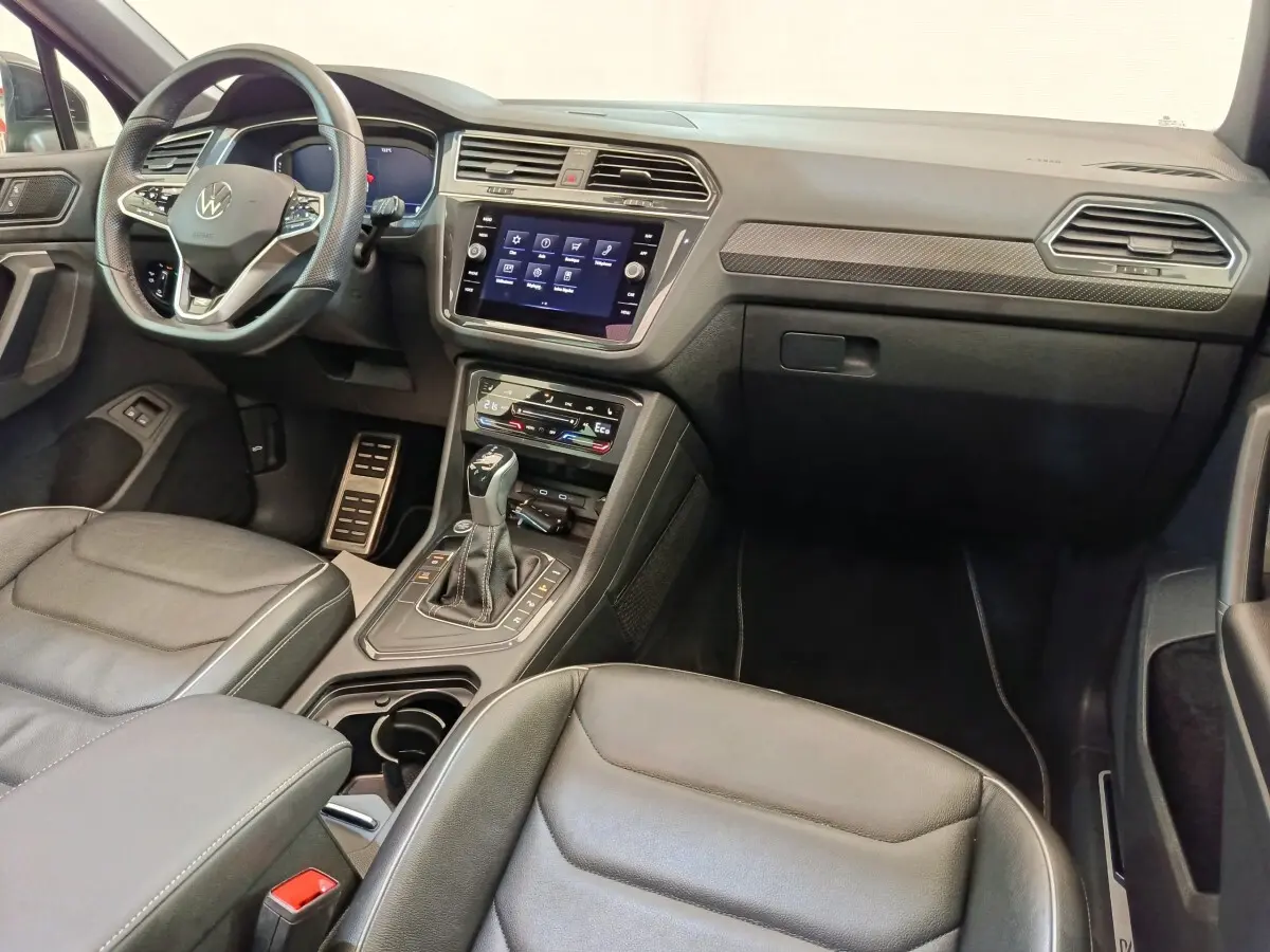 Vue intérieure avant droite du Volkswagen Tiguan 1.4 eHybrid 2023, tableau de bord noir avec écran tactile central et volant cuir multifonctions.