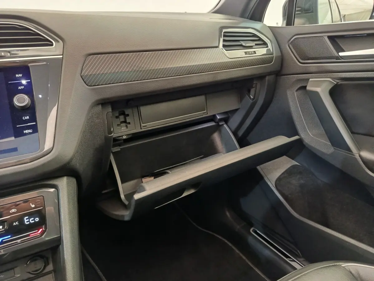 Intérieur du Volkswagen Tiguan 2023, vue côté passager sur la boîte à gants ouverte et tableau de bord noir.