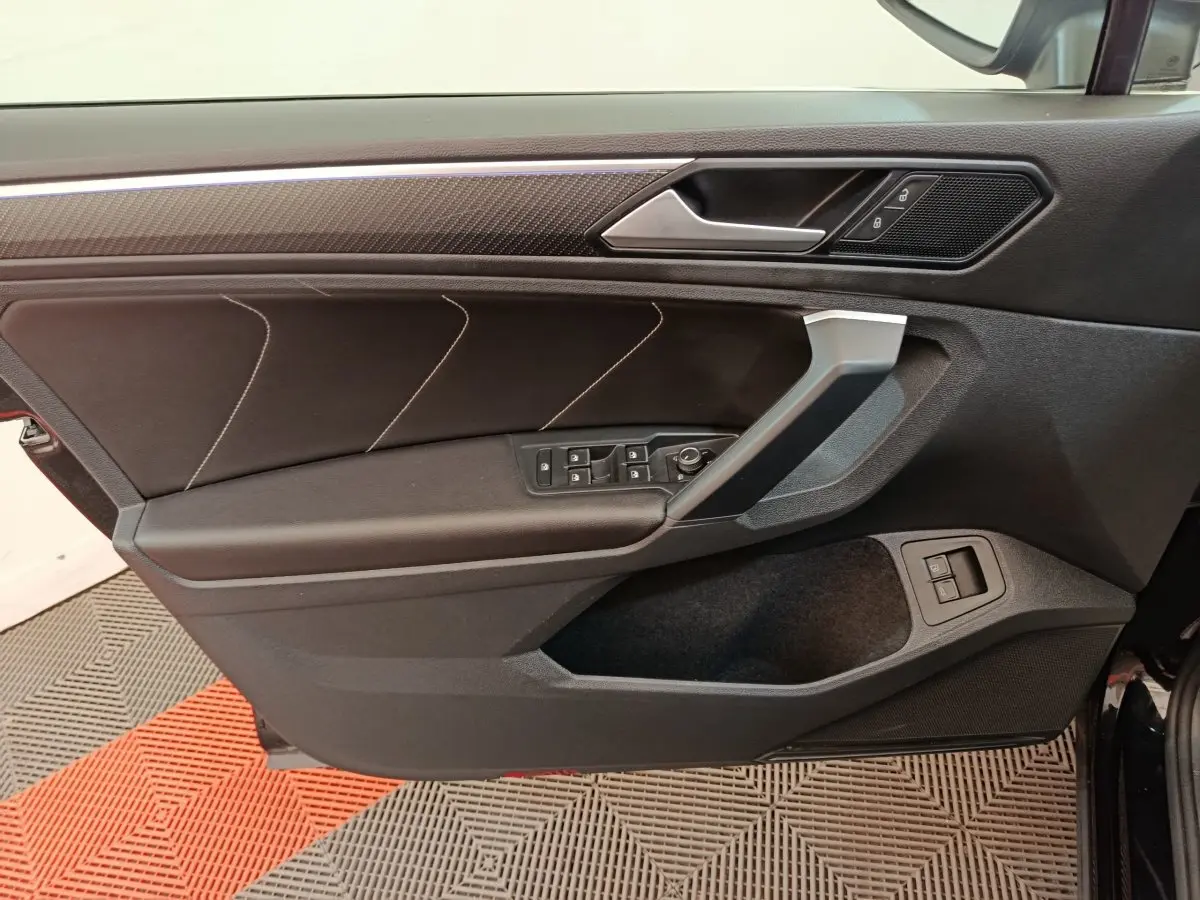 Vue intérieure de la porte avant gauche du Volkswagen Tiguan noir, avec commandes électriques et insert décoratif.