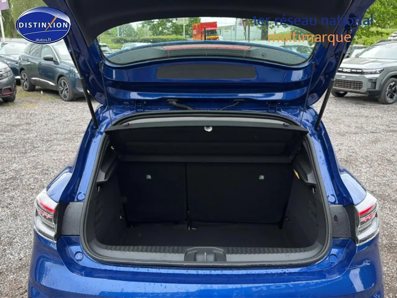 Coffre ouvert vu de l'arrière d'une Renault Clio V bleu iron, avec feux arrière LED visibles.