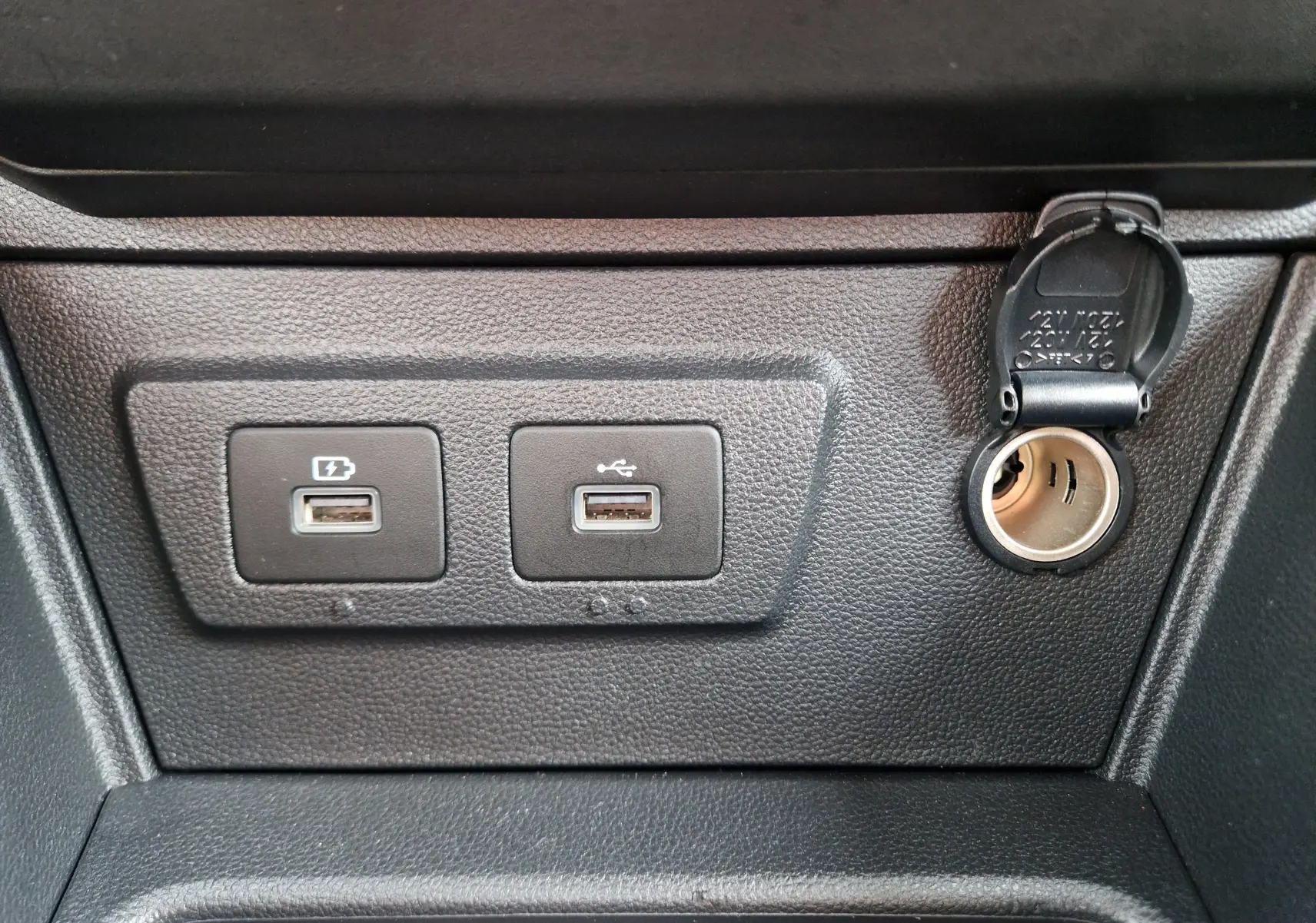 Gros plan sur les ports USB et prise 12V du tableau de bord noir du Dacia Duster blanc 4x4 2023.