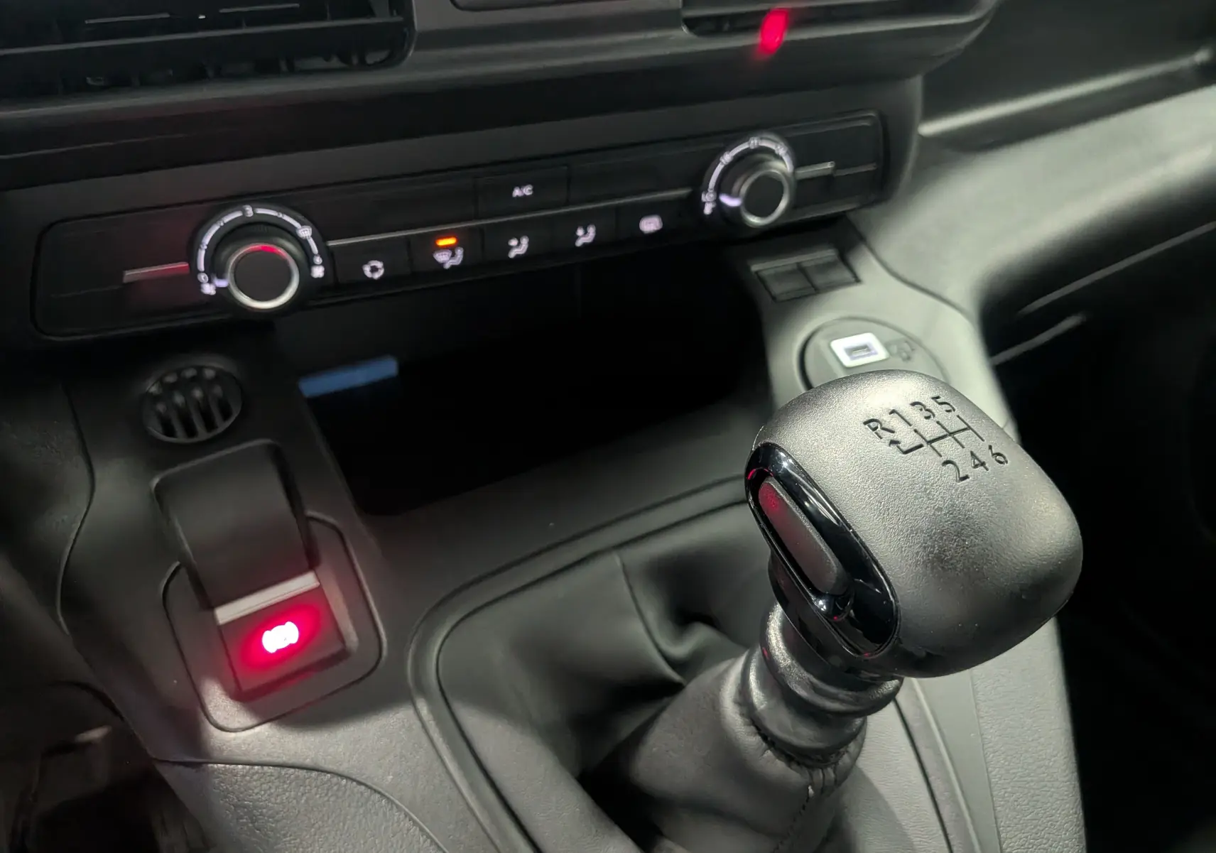 Gros plan sur le levier de vitesses manuel noir du Citroën Berlingo blanc, avec les commandes de climatisation en arrière-plan.