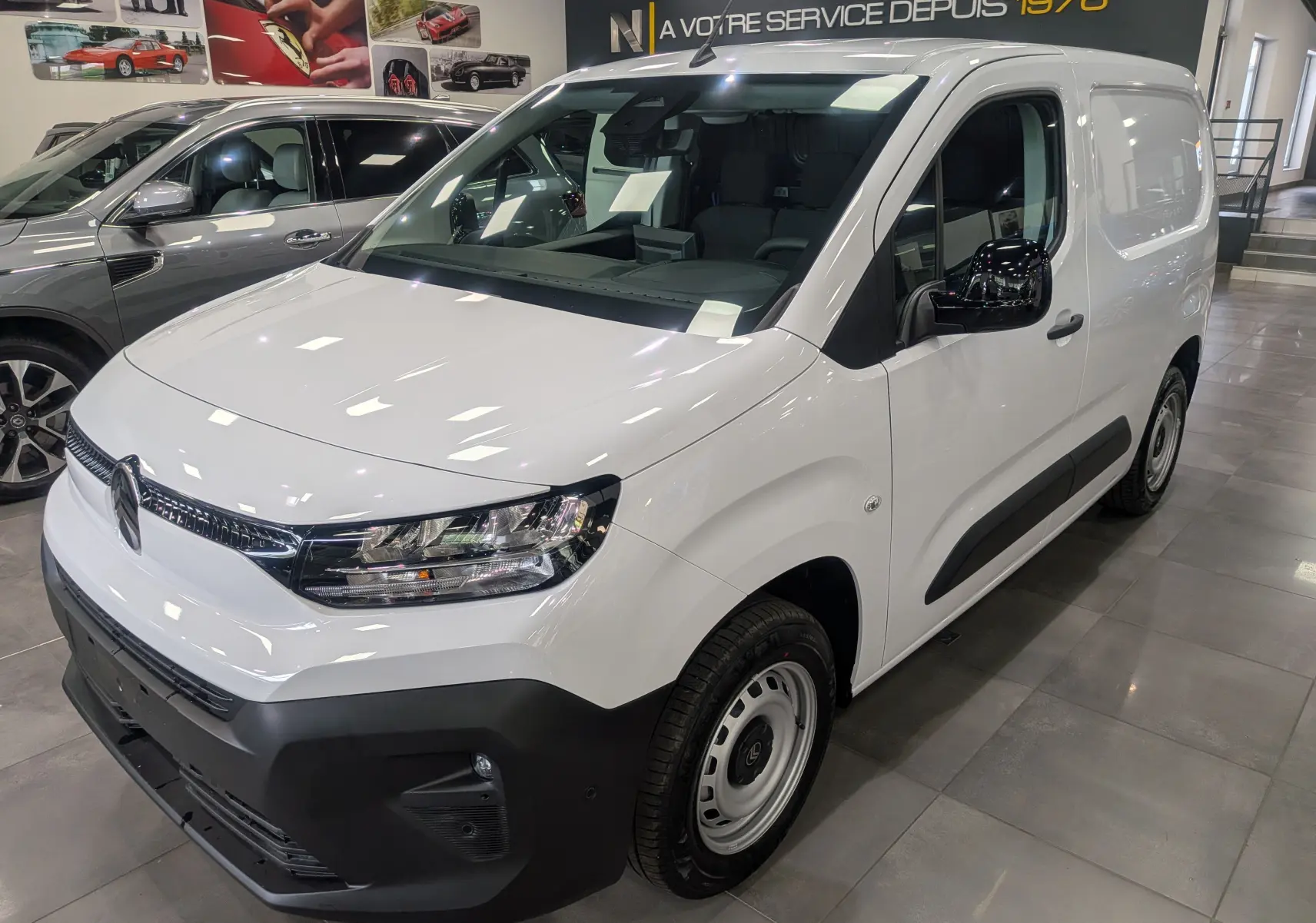 Vue 3/4 avant d'un Citroën Berlingo Van blanc 2025 avec pare-chocs noir et jantes acier en intérieur showroom.