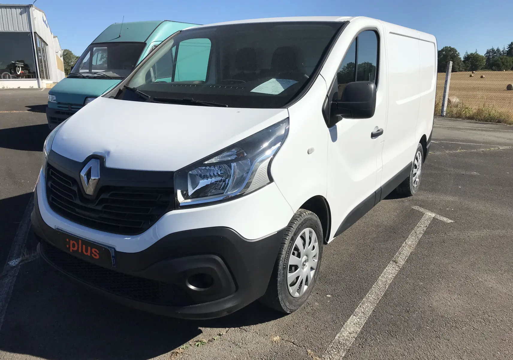 Renault Trafic Fourgon blanc vu en 3/4 avant droit, avec calandre noire et jantes tôles sur parking extérieur.