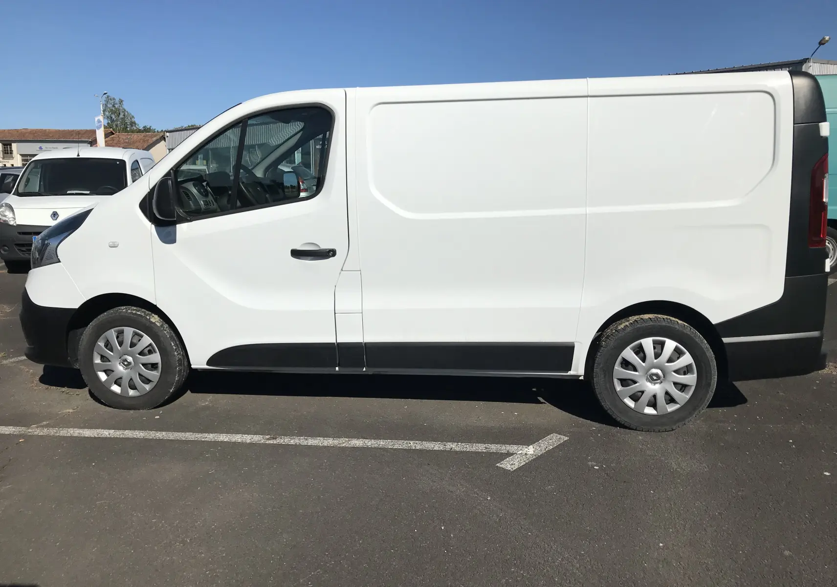 Fourgon Renault Trafic blanc vu de profil côté gauche, avec jantes argentées et pare-chocs noirs.