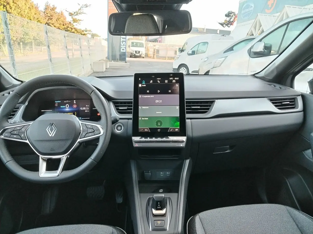 Vue intérieure frontale du Renault Captur E-Tech gris Cassiopée, tableau de bord moderne avec écran tactile vertical et volant multifonction.