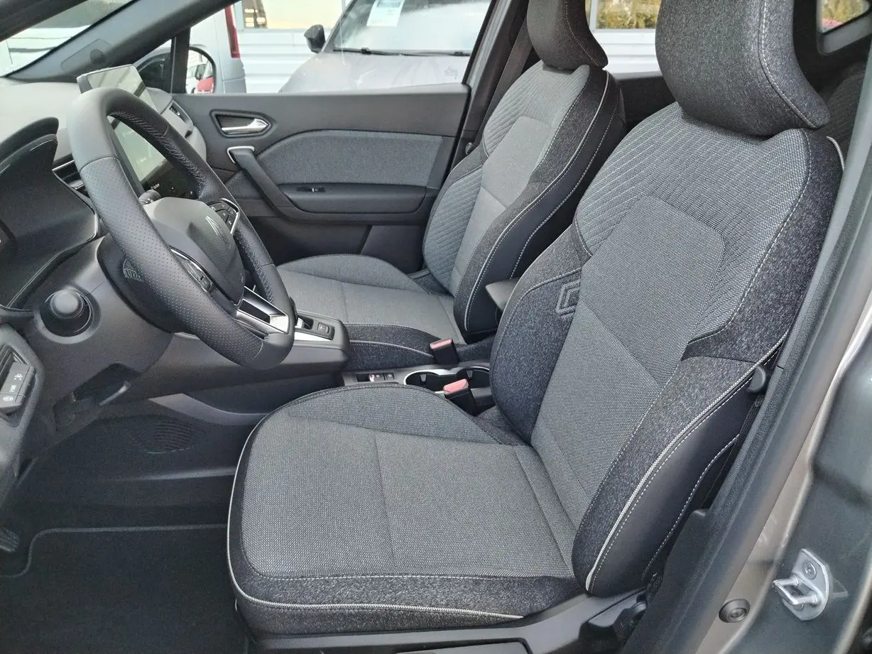 Vue intérieure côté conducteur du Renault Captur 2025, sièges tissu gris avec surpiqûres blanches et volant cuir noir.
