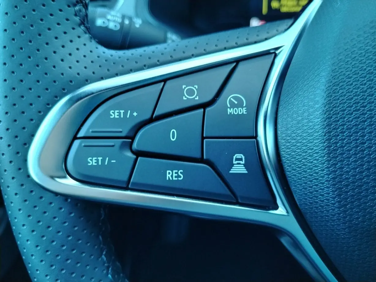 Gros plan sur les commandes du volant perforé du Renault Captur E-Tech gris cassiopée, boutons de régulateur et mode de conduite.