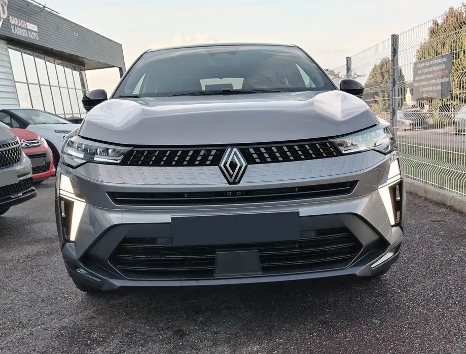 Vue frontale du Renault Captur E-Tech gris Cassiopée avec toit noir, feux LED verticaux allumés, calandre moderne.