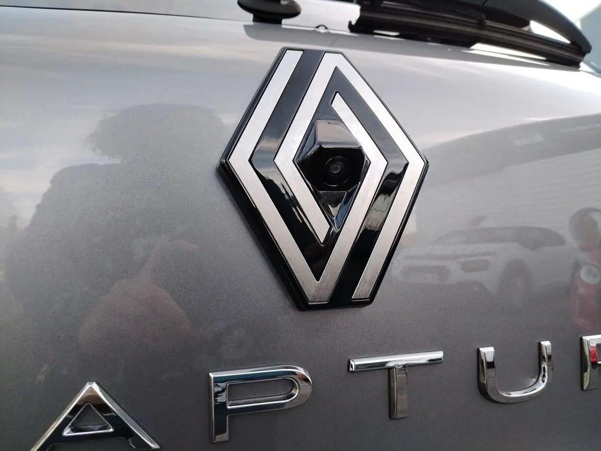 Gros plan sur le logo Renault avec caméra intégrée sur la malle arrière d'un Captur gris Cassiopée 2025.