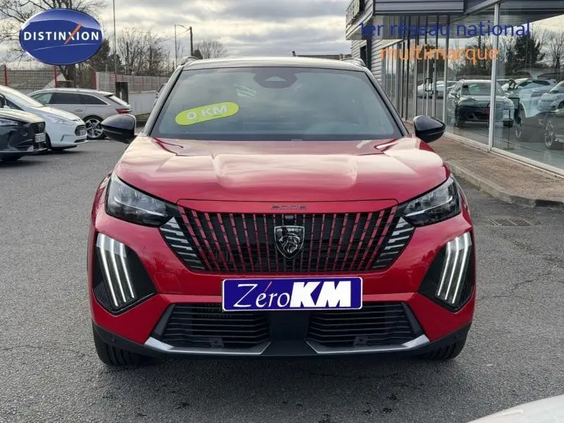 Vue avant d’un Peugeot 2008 rouge avec feux LED verticaux et calandre noire distinctive, en extérieur sur parking.