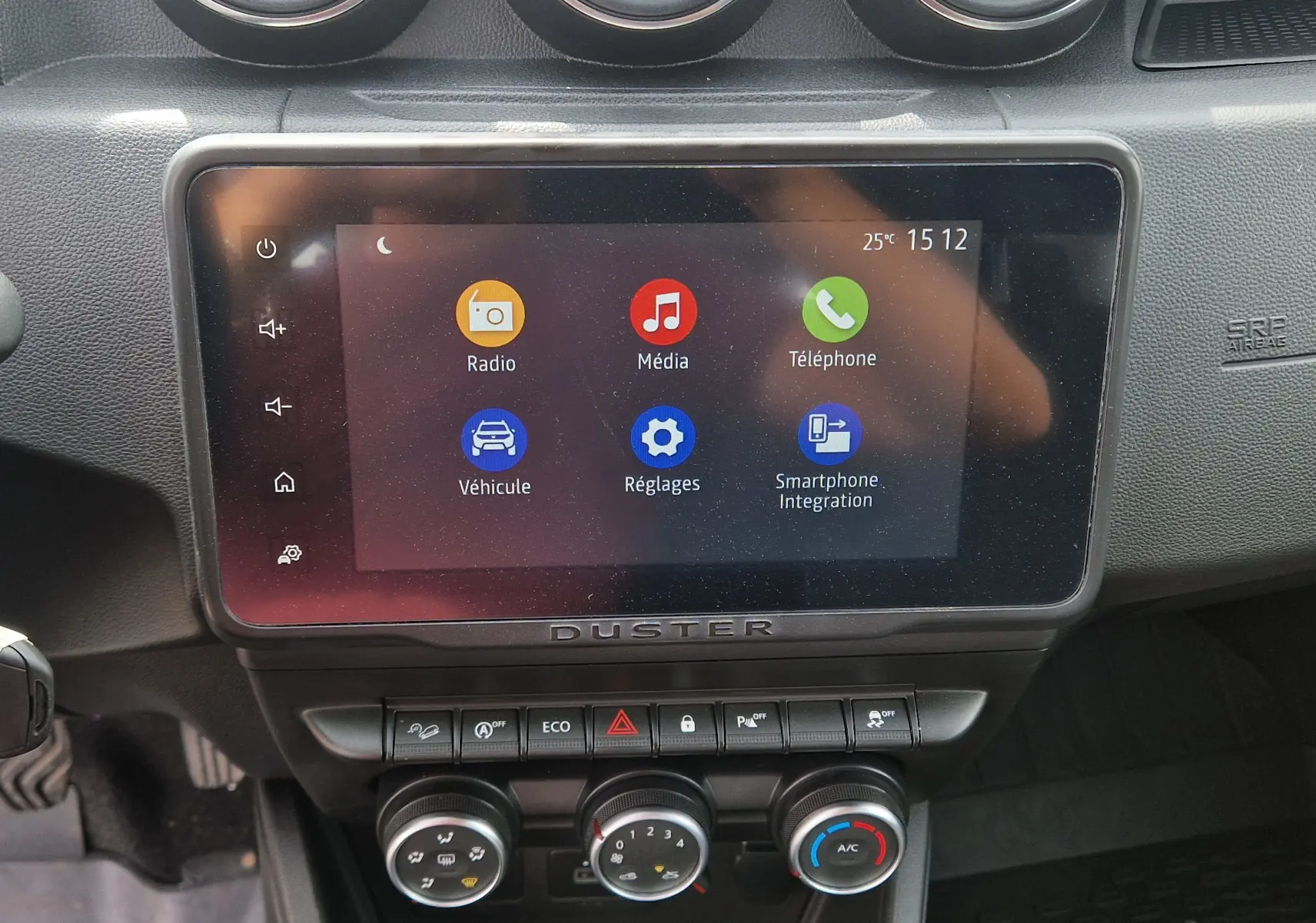 Vue rapprochée de l’écran tactile central du tableau de bord du Dacia Duster 2023 avec commandes climatisation et boutons fonctionnels.