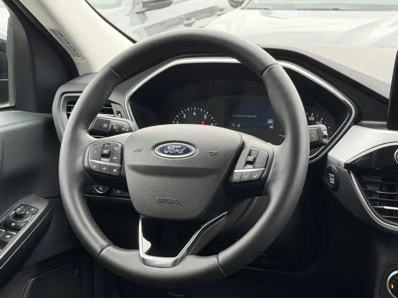 Vue rapprochée du volant noir du Ford Kuga 2024 1.5 EcoBoost Titanium, avec commandes intégrées et tableau de bord partiellement visible.