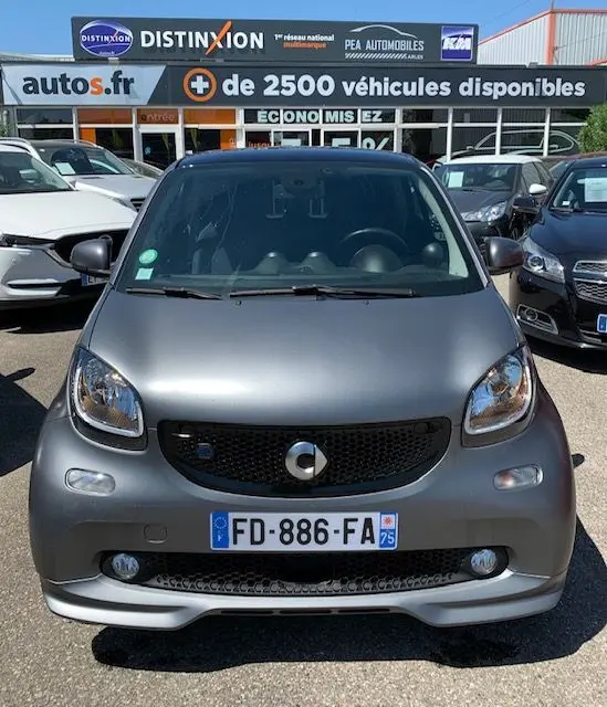 Vue avant d'une Smart Fortwo Coupé électrique gris mat, version Brabus Style, stationnée en extérieur devant un concessionnaire.