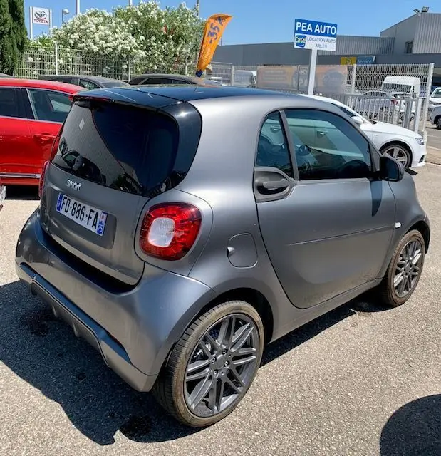 Vue 3/4 arrière droite d'une Smart Fortwo électrique Brabus style gris métallisé avec jantes sport et toit noir.