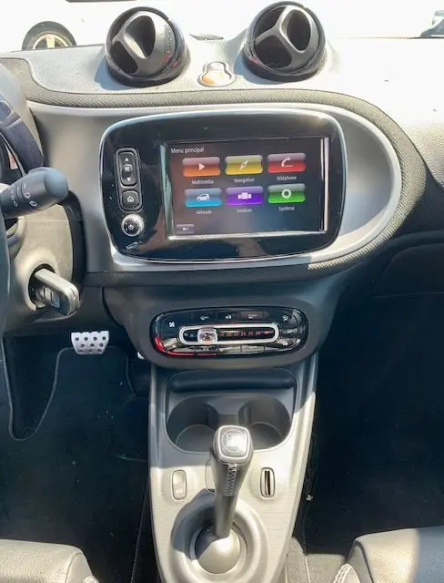 Vue intérieure centrée sur la console centrale d'une Smart Fortwo électrique grise, avec écran tactile et levier de boîte automatique.