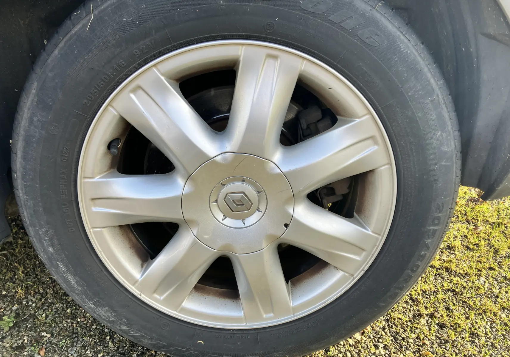 Gros plan sur la roue avant gauche de la Renault Laguna gris vert 2008 avec jante alliage et logo Renault central.