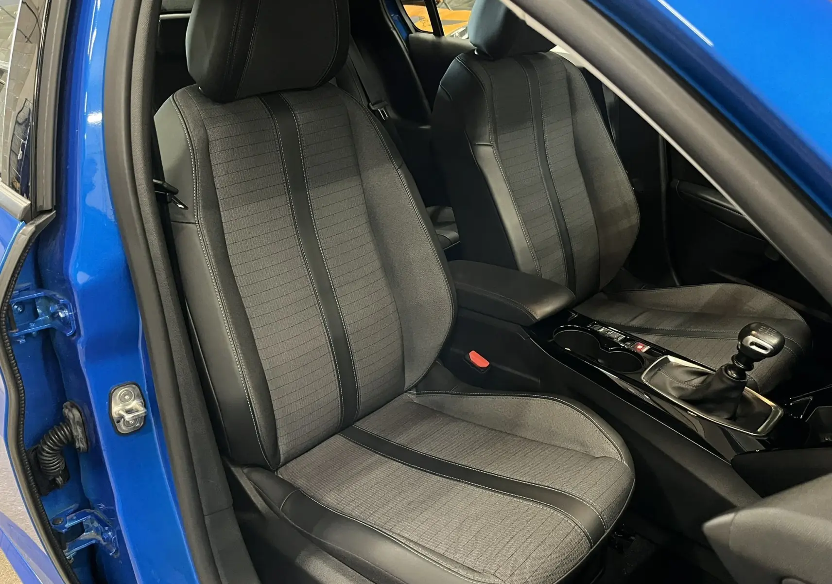 Vue intérieure côté conducteur de la Peugeot 208 Bleu Vertigo avec sièges gris et levier de vitesse manuel visible.