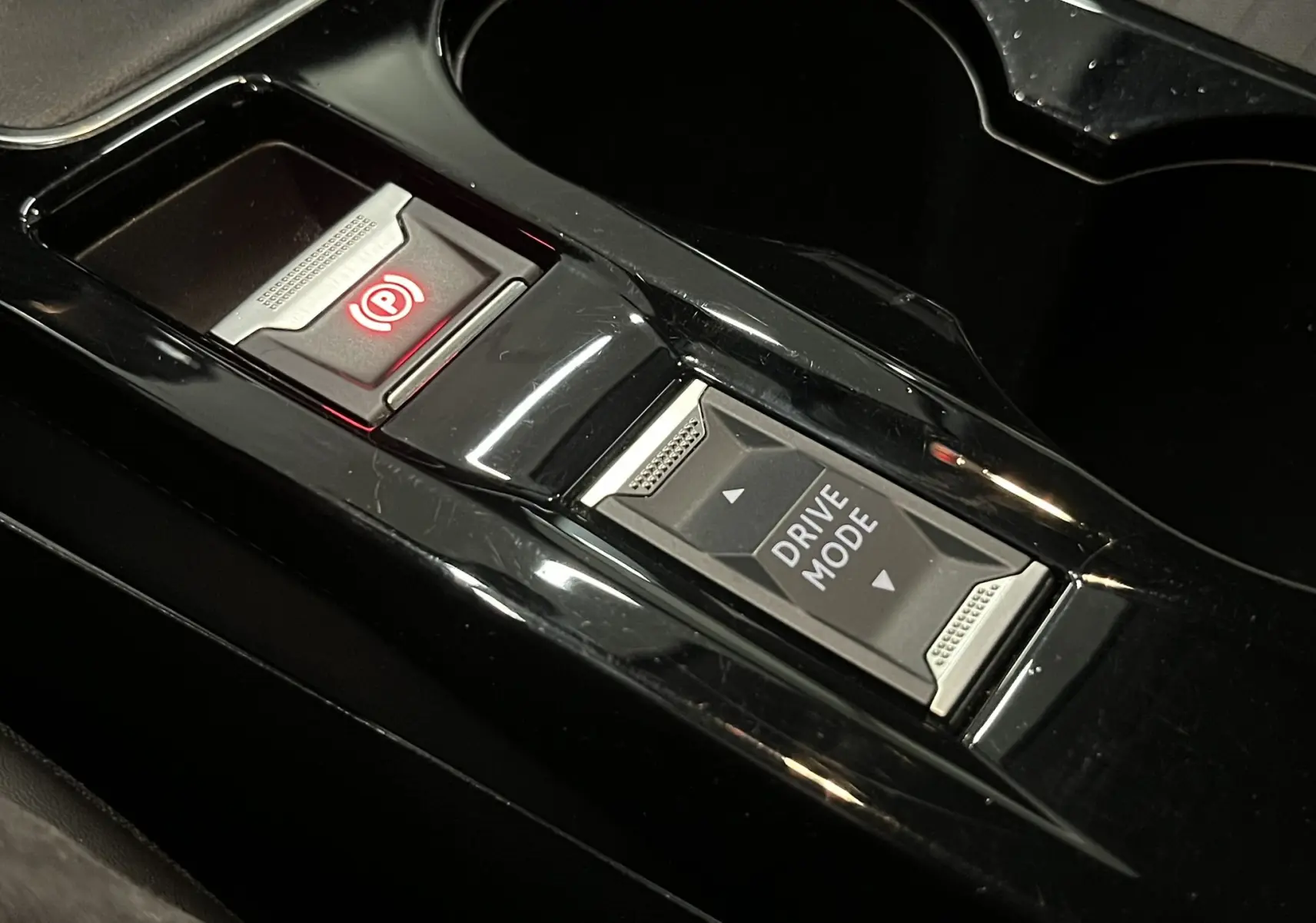 Gros plan sur la console centrale noire brillante de la Peugeot 208 1.5 BlueHDi, avec bouton frein à main électronique et sélection drive mode.
