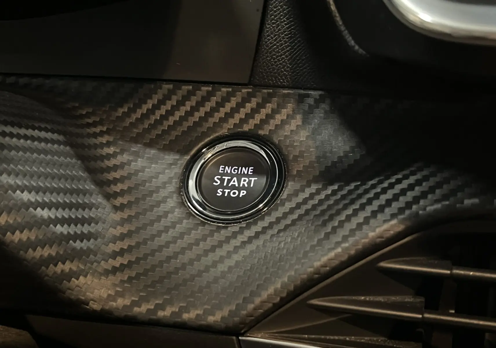 Bouton start/stop moteur sur tableau de bord avec finition carbone dans l'habitacle d'une Peugeot 208 Bleu Vertigo.