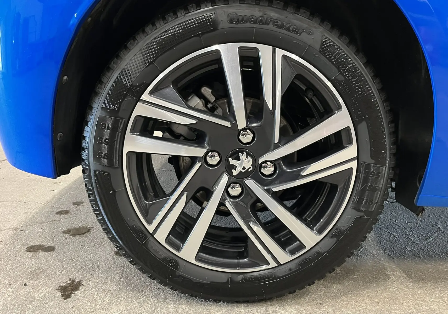 Gros plan sur la jante alliage bicolore noire et argentée d'une Peugeot 208 Bleu Vertigo, côté avant droit.