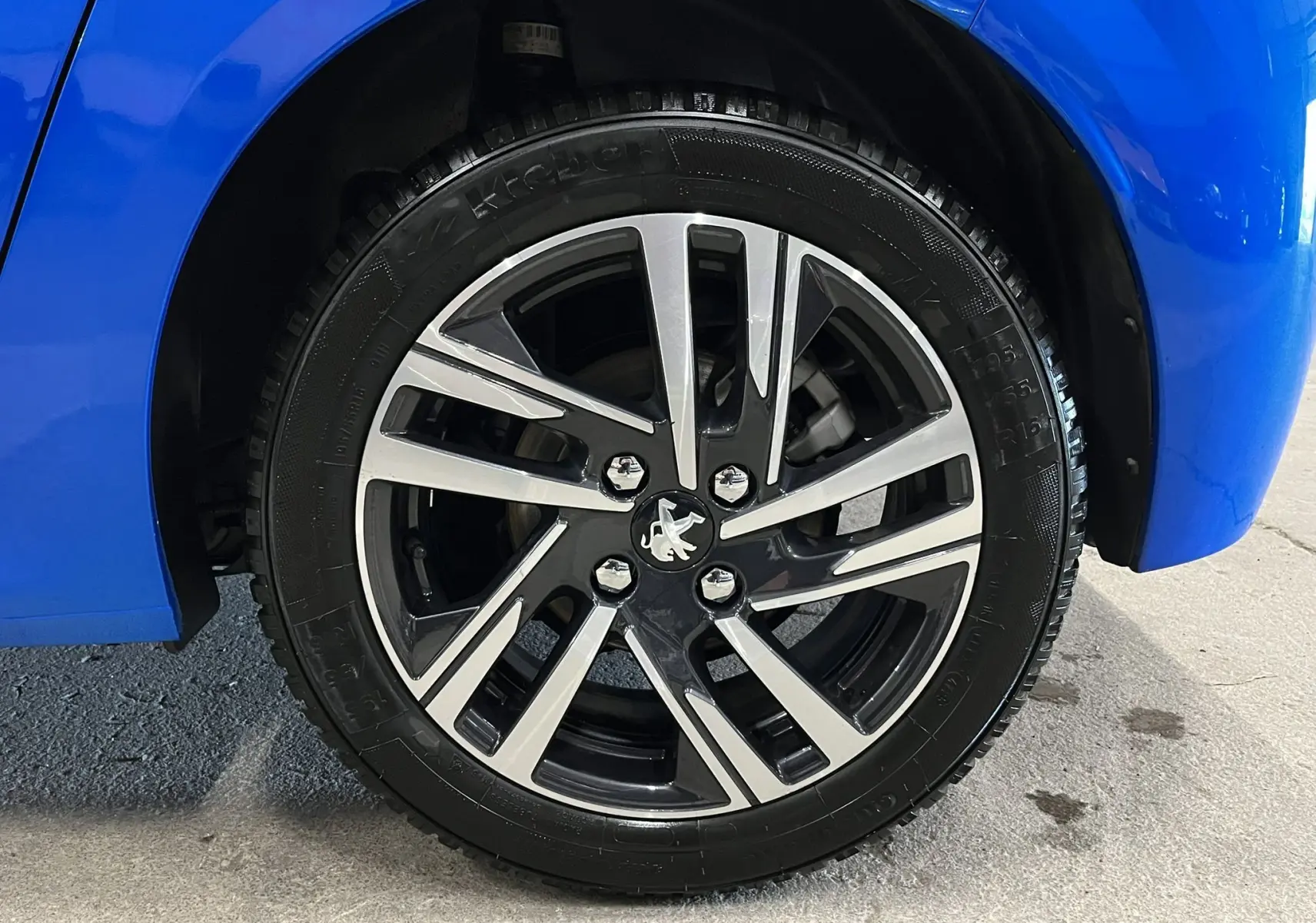 Gros plan sur la roue avant droite d'une Peugeot 208 Bleu Vertigo avec jante alliage bicolore moderne.