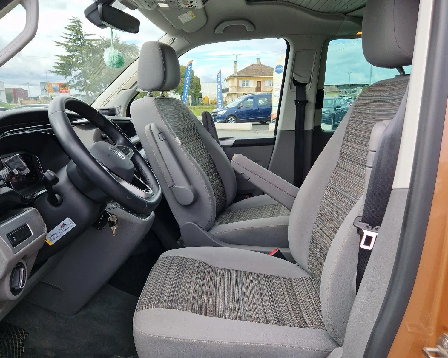 Vue intérieure côté conducteur du Volkswagen California Cooper bronze 2021, sièges gris à motifs rayés et toit relevable fermé.