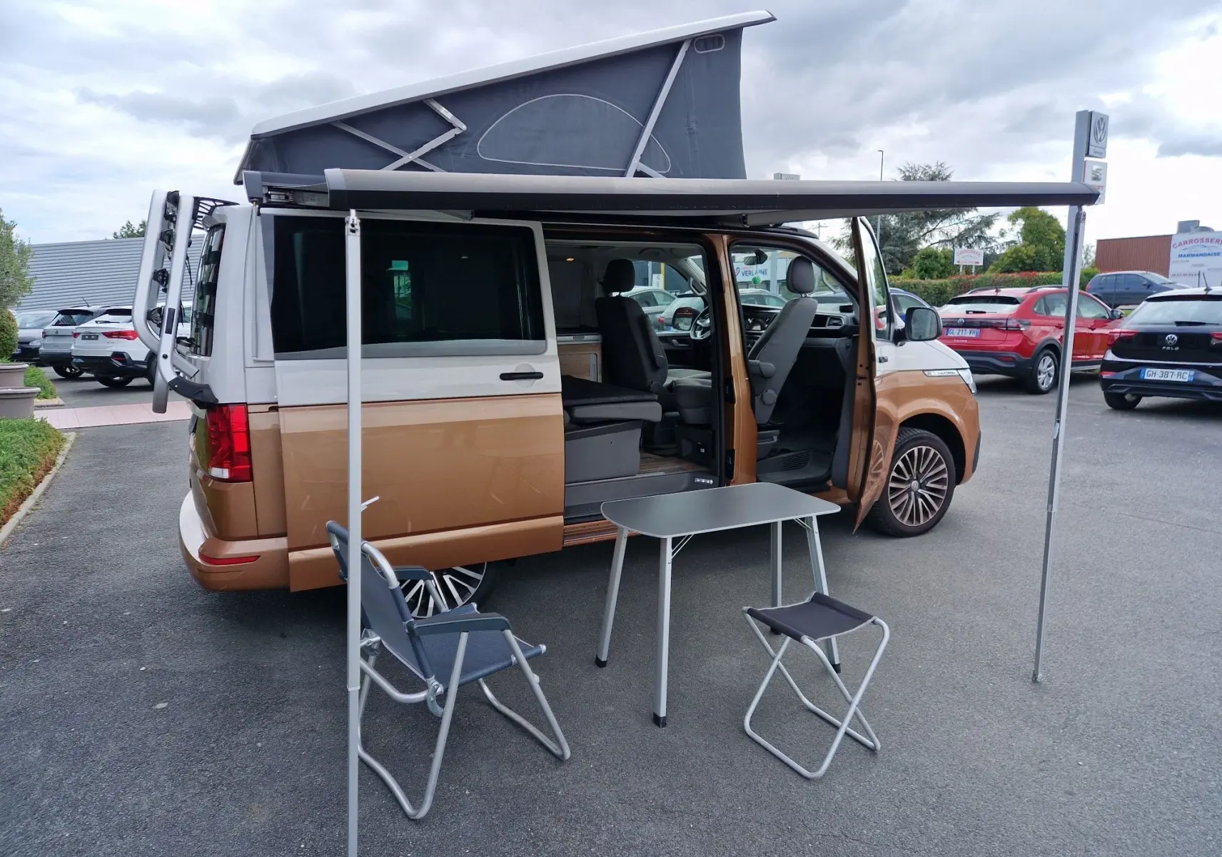 Vue latérale droite d'un Volkswagen California Cooper bronze 2021 avec toit relevé et auvent déployé, aménagé pour camping.