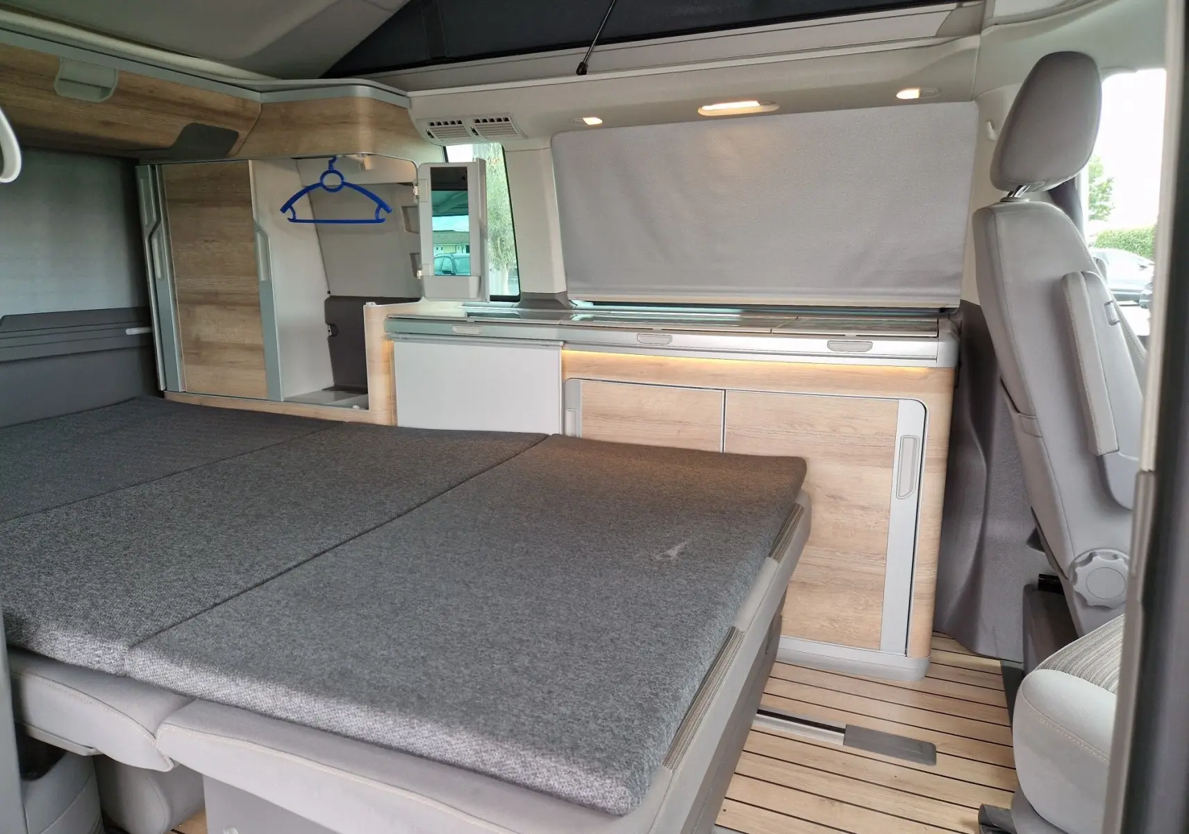 Intérieur du Volkswagen California 2.0 TDi 150 ch Coast 2021, vue latérale sur le coin nuit avec lit déplié et rangements bois clair.