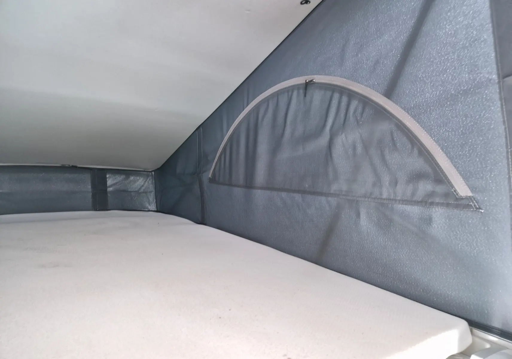 Détail intérieur du couchage avec fenêtre en demi-lune dans le toit relevable du Volkswagen California Cooper bronze.