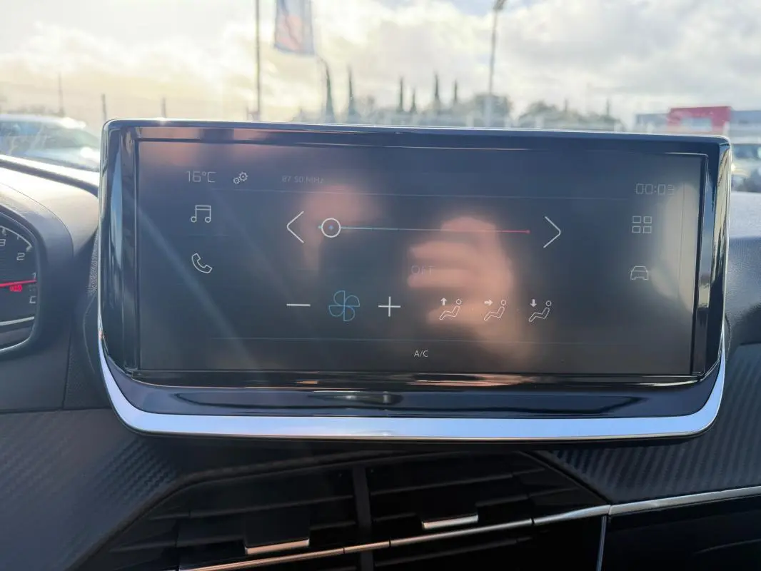 Écran tactile du tableau de bord de la Peugeot 208 jaune, vue frontale intérieure avec commandes climatisation visibles.