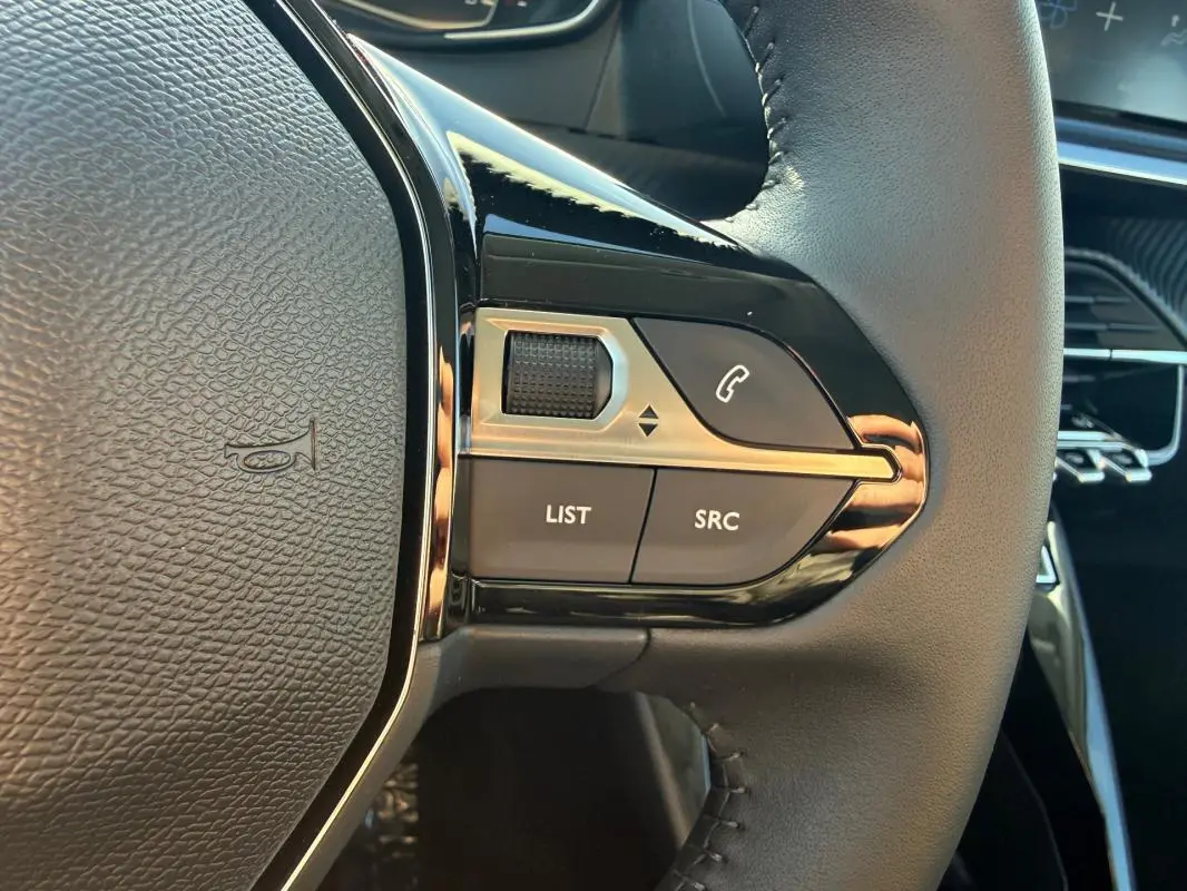Gros plan sur les commandes gauche du volant noir de la Peugeot 208 jaune, avec boutons LIST, SRC et téléphone.