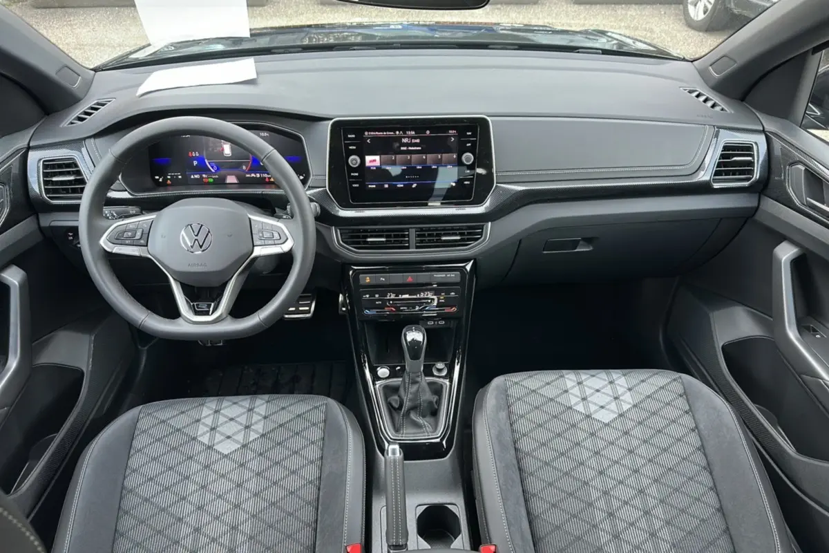 Vue intérieure frontale du Volkswagen T-Cross TSI 116 DSG7 R-Line 2025, sièges tissu gris à motifs géométriques et tableau de bord numérique.