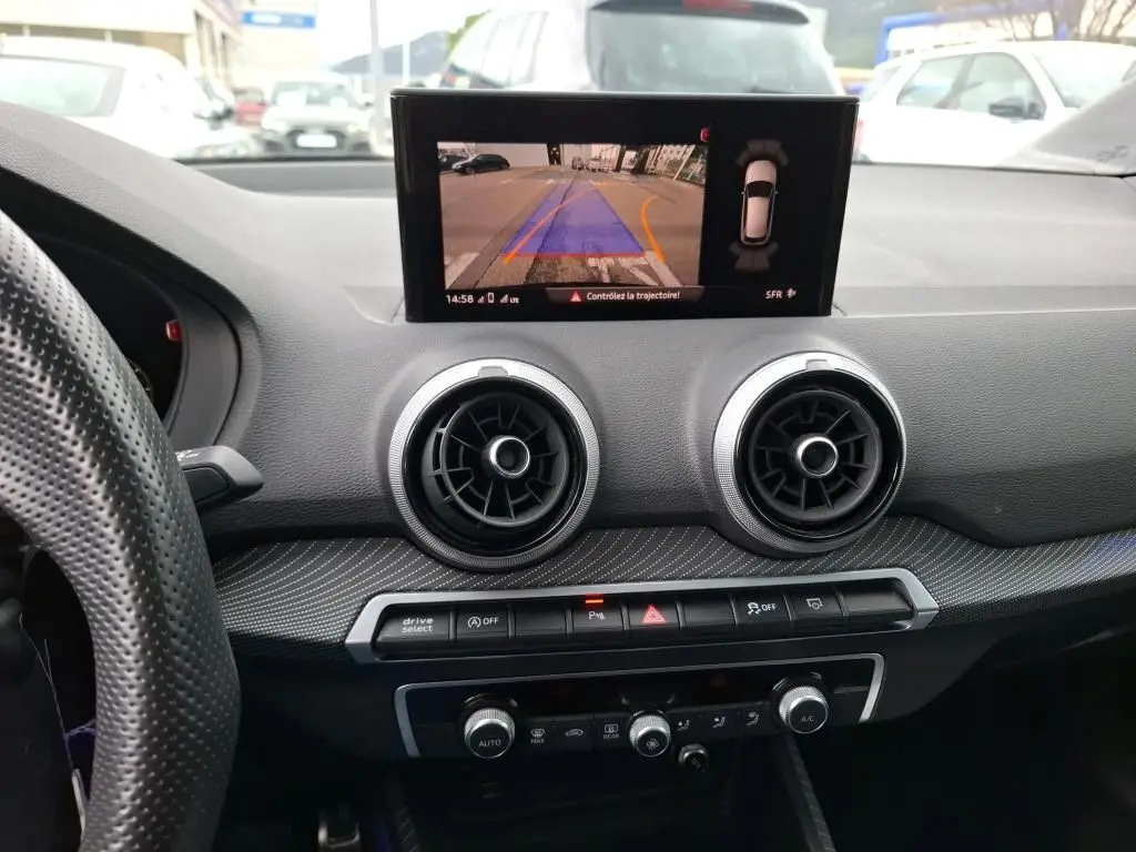 Vue intérieure du tableau de bord noir d'Audi Q2 2023 avec écran affichant la caméra de recul et aérateurs ronds centraux.