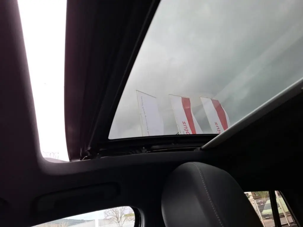 Vue intérieure du toit ouvrant panoramique ouvert sur Audi Q2 noir, avec appui-tête avant visible et ciel nuageux.