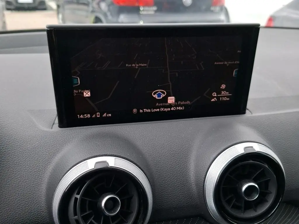 Écran GPS central et aérateurs ronds argentés du tableau de bord d’un Audi Q2 2023 noir, vue intérieure frontale.