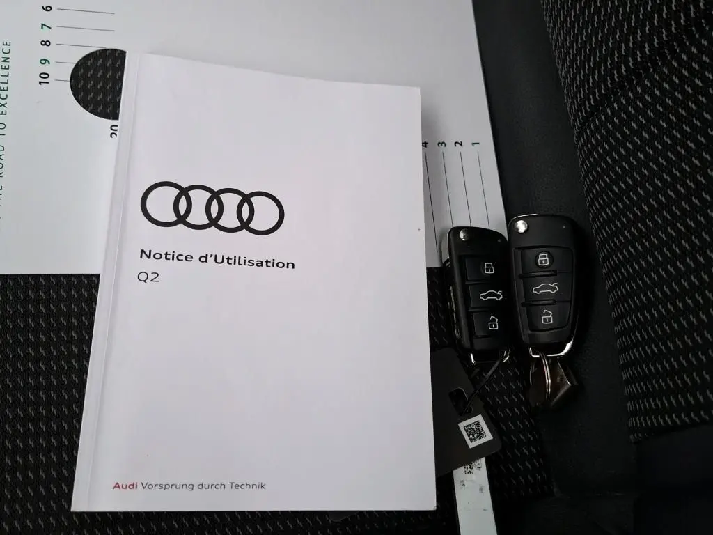 Manuel d'utilisation Audi Q2 posé sur siège tissu noir avec deux clés de voiture noires à côté.
